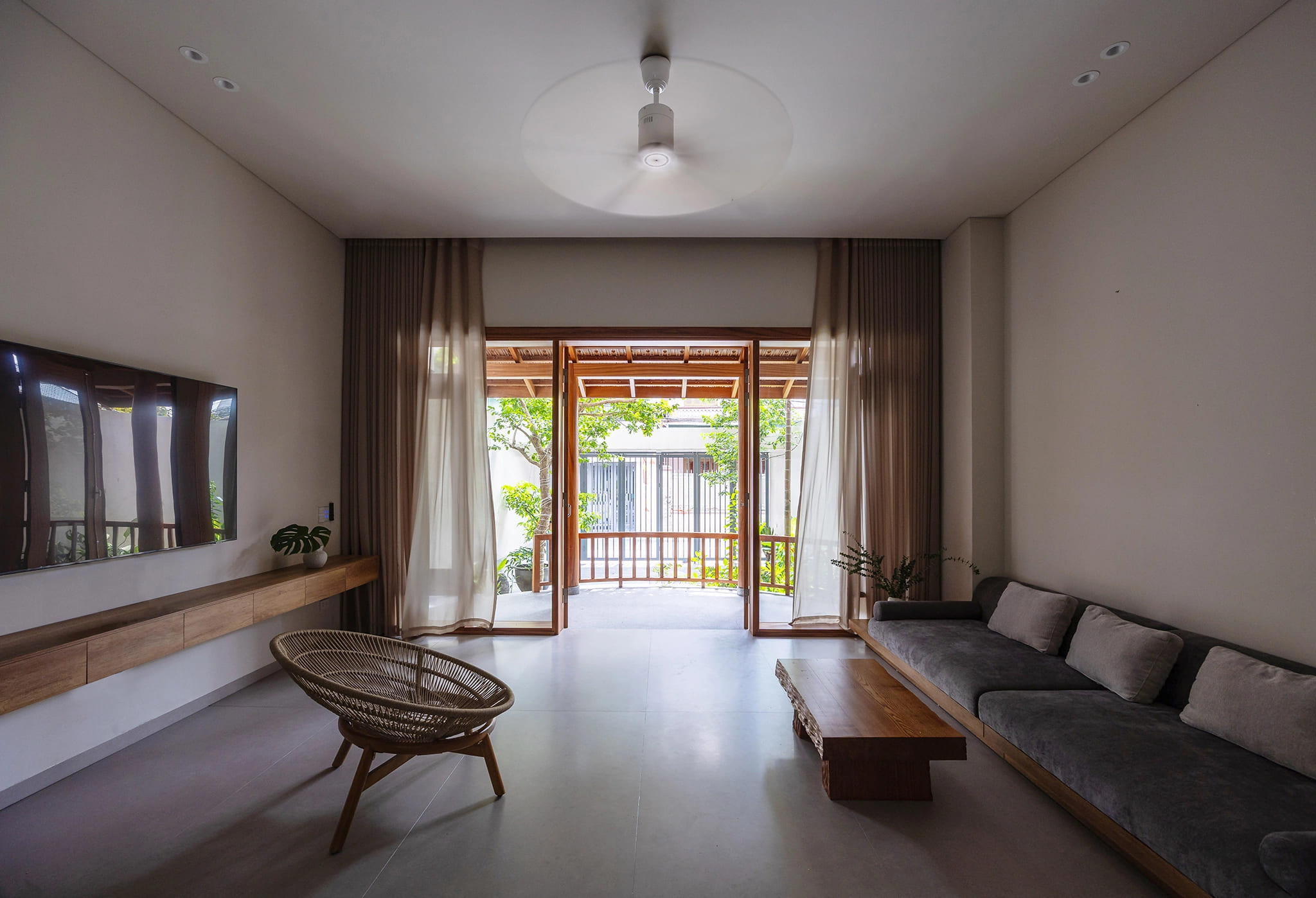 Từ hiên nhìn vào, phòng khách rộng mở với tông màu be và nâu gỗ chủ đạo, tạo cảm giác ấm áp